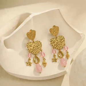 Detailansicht von herzförmigen Goldohrringen mit rosa Perlen und Meeresanhängern.