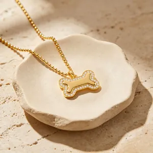 Gros plan d'un pendentif en forme d'os doré avec bordure en cristal sur une chaîne à billes.