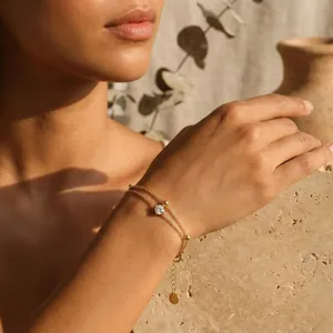 Detail of a minimalist double-layered gold bracelet with a single zircon on a woman's wrist.
