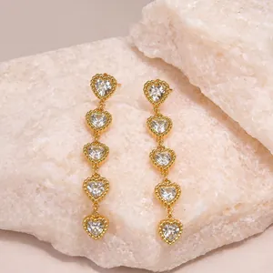 Vue détaillée de boucles d'oreilles pendantes en acier doré avec cinq cœurs en cristal
