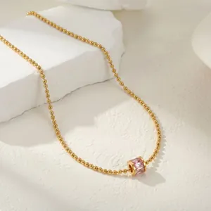 Primer plano de un collar de cuentas doradas minimalista con colgante de cristal rosa