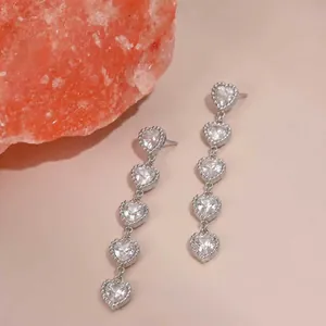 Détail de boucles d'oreilles pendantes argentées avec cinq cœurs sertis de cristaux.