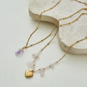Close-up of stainless steel amethyst and rose quartz heart pendant necklaces on a stone tray