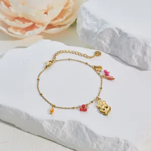 Detail eines vergoldeten Armbands mit bunten Blumen- und Herzanhängern auf Stein