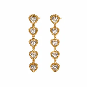 Détail de boucles d'oreilles pendantes dorées avec cinq cœurs en cristal empilés.