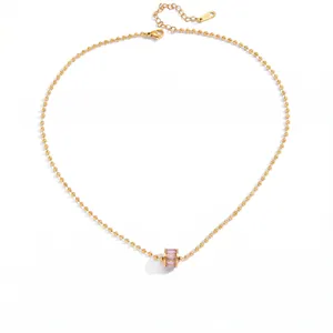 Detalle de un collar de cadena de bolas dorada minimalista con un colgante de cristal rosa
