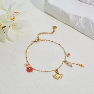 Detailed view of a gold-plated bracelet with enamel floral and ginkgo leaf charms.