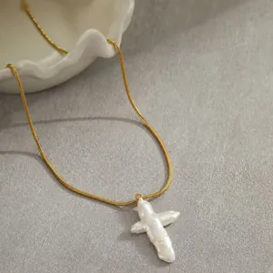 Détail d'une chaîne serpent dorée avec un pendentif croix en perle baroque irrégulière.