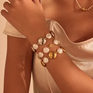 Close-up detail of elegant baroque pearl and polished metal disc bracelets on a wrist