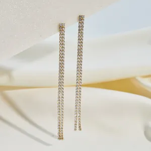 Macro detail of long gold-plated double-strand rhinestone tassel earrings for women.