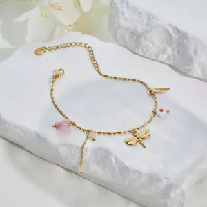 Detailaufnahme eines vergoldeten Edelstahl-Armbands mit Libellen- und Blumenanhängern