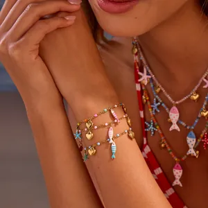Nahaufnahme von Edelstahl-Armbändern mit Emaille-Fisch- und Herz-Anhängern am Modell.
