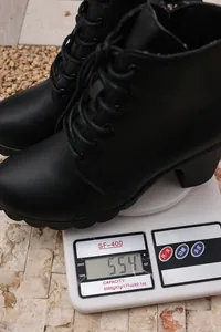 Macro view of black lace-up ankle boots showing a weight of 554g on a scale