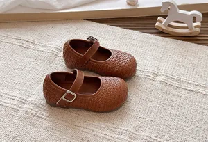 Zapatos Mary Jane trenzados marrones para niñas con hebilla sobre alfombra beige