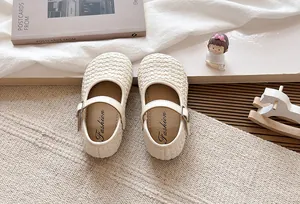 Primer plano de zapatos planos trenzados crema para niñas con detalle de correa con hebilla