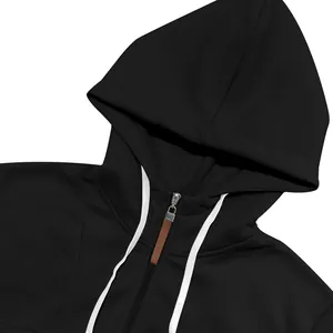 Detalle de una sudadera con capucha negra de gramaje pesado con cremallera y cordones blancos.
