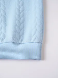 Close-up of light blue cable-knit sweater detail showing ribbed hem and knit texture.