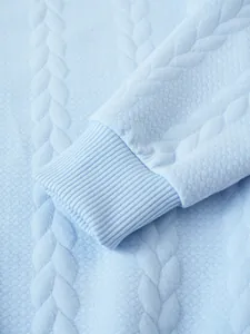 Macro view showing the soft light blue jacquard texture and ribbed cuff of this men's sweater