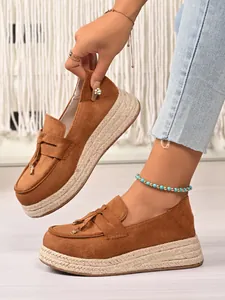 Close-up of brown suede platform loafers with jute-wrapped soles and tassel detail.