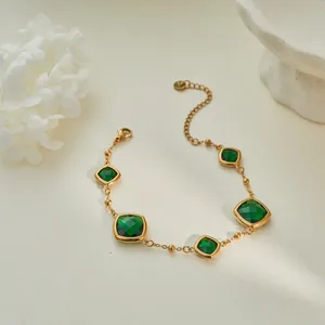 Primer plano de pulsera de acero de titanio dorado con cinco circonitas verdes cuadradas