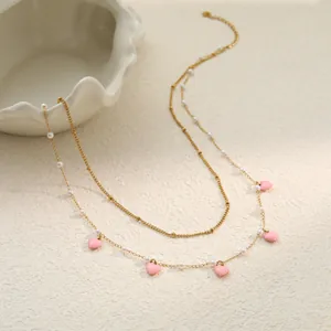 Nahaufnahme von rosa Emaille-Herzanhängern und weißen Perlen an goldener Kette