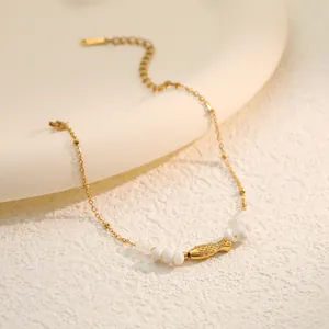 Detail view of a gold stainless steel bracelet with white shell beads and a fish charm