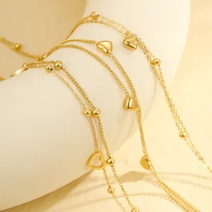Primer plano de una tobillera multicapa de acero inoxidable dorado con dijes de corazón