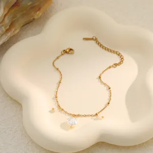 Detail view of a gold-toned stainless steel bracelet with a white shell charm and pearls