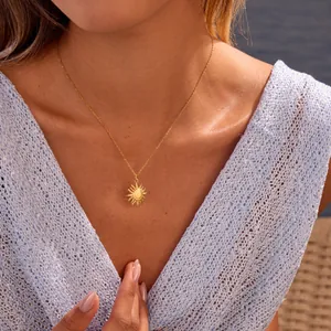 Dettaglio di una collana con ciondolo a sole dorato su modella con top in maglia azzurra