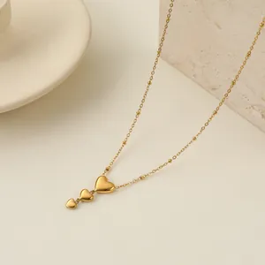Dettaglio ravvicinato di una collana in acciaio dorato con tre ciondoli a forma di cuore.