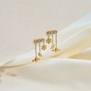 Close-up of gold stainless steel dangle earrings with bee and flower charms.