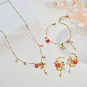 Detailed view of gingko leaf and red flower charms on necklace, bracelet, and earrings