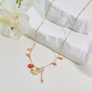 Close-up of gold necklace with ginkgo leaf and red flower charms