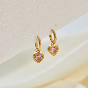 Primer plano de pendientes de aro de acero dorado con dije de cristal rosa en corazón.