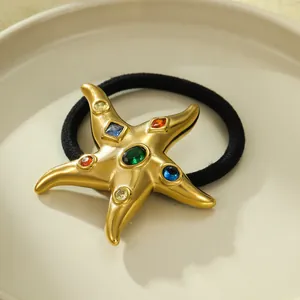 Macro view of a golden starfish hair tie featuring vibrant crystals and a black elastic rope
