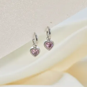 Vista detallada de pendientes de aro de acero con colgantes de corazón en cristal rosa.