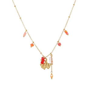 Detailed view of elegant gold necklace featuring ginkgo leaf charm and red floral beads