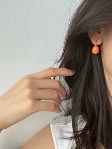 Détail d'une boucle d'oreille goutte orange vif portée par un mannequin aux cheveux noirs.