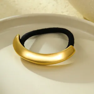Close-up detail of a minimalist 18k gold crescent metal hair tie with black elastic band