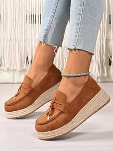 Detail view of brown suede platform loafers with jute espadrille sole and tassel accents.