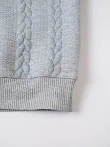 Detailed view of gray cable-knit texture and ribbed hem on a men's winter sweater