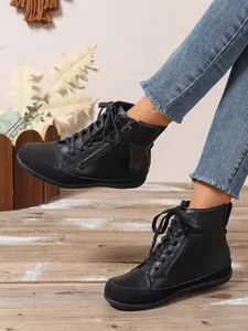Botines negros cómodos con cordones y cremallera lateral sobre suelo de madera real