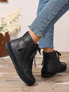 Detalle de botines negros planos con cremallera lateral sobre suelo de madera