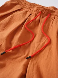 Detalle del cordón rojo y la cintura elástica en pantalones de lino naranja para hombre