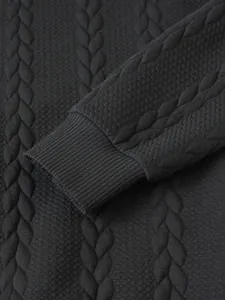 Close-up of black men's cable knit sweater showing ribbed cuff and jacquard texture