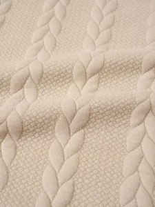 Macro detail of men's beige cable knit sweater showing intricate jacquard texture