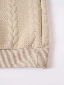 Macro view of beige cable-knit sweater fabric showing intricate patterns and ribbed hem