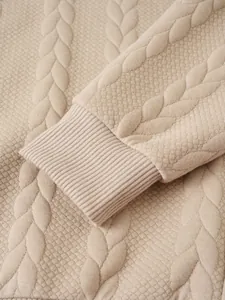 Close-up detail of beige cable knit sweater showing waffle texture and ribbed cuff