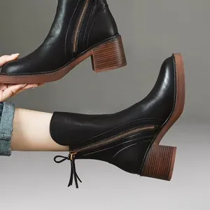 Detailed view of black leather ankle boots with chunky brown heel and side zipper.