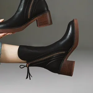 Close-up of black chunky heel leather ankle boots with side zipper and tassel detail